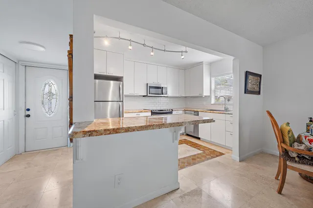 a kitchen with stainless steel appliances granite countertop a stove top oven a sink a refrigerator a dining table and chairs with wooden floor