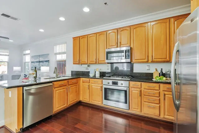 a kitchen with stainless steel appliances granite countertop wooden cabinets a sink and dishwasher with wooden floor