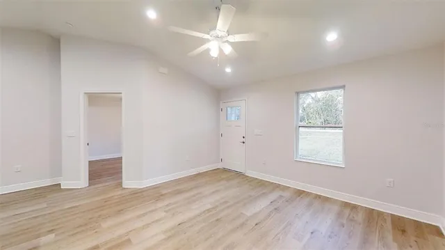 an empty room with wooden floor fan and windows