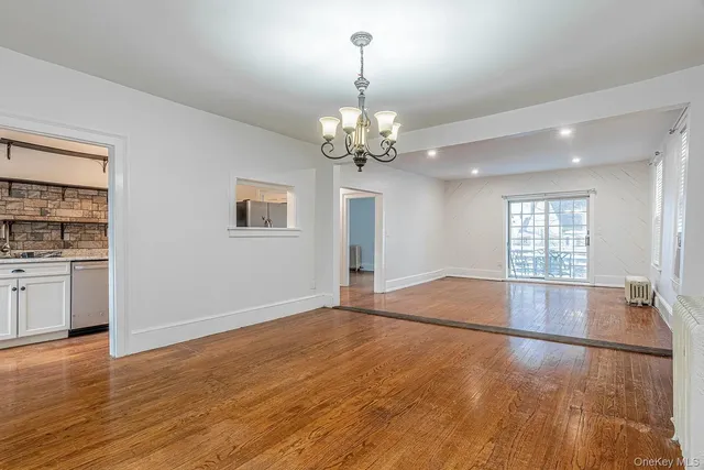 an empty room with wooden floor chandelier and windows