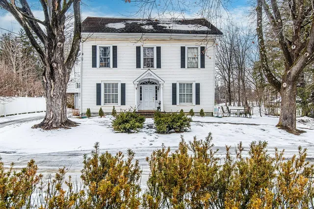 a front view of a house with a yard covered with snow and trees