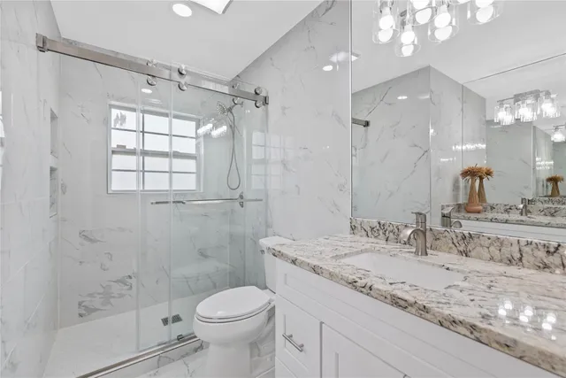 a bathroom with a granite countertop sink a toilet a mirror a vanity and shower