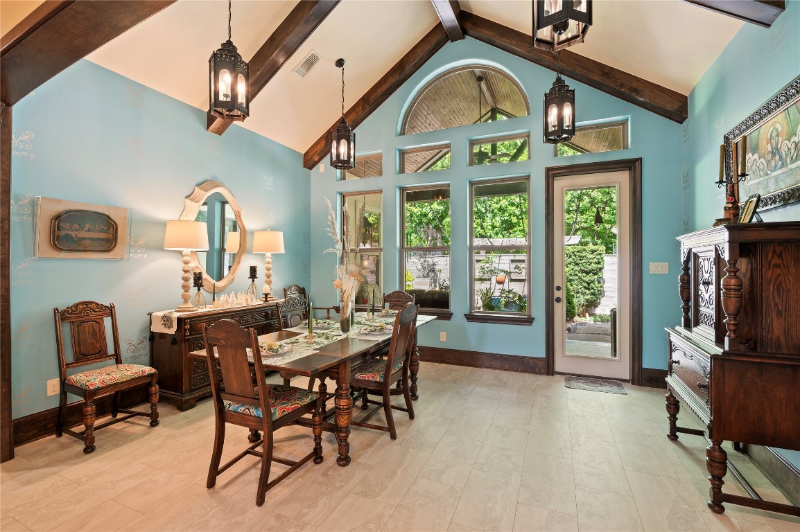 2201 Water Way Seabrook, TX 77586 - Photo 13 of 48 This inviting dining room features vaulted ceilings with exposed beams, elegant pendant lights, and a large arched window that allows natural light to fill the space. The room is painted in a soothing blue, complemented by dark wood furniture and accents, creating a warm and classic ambiance.