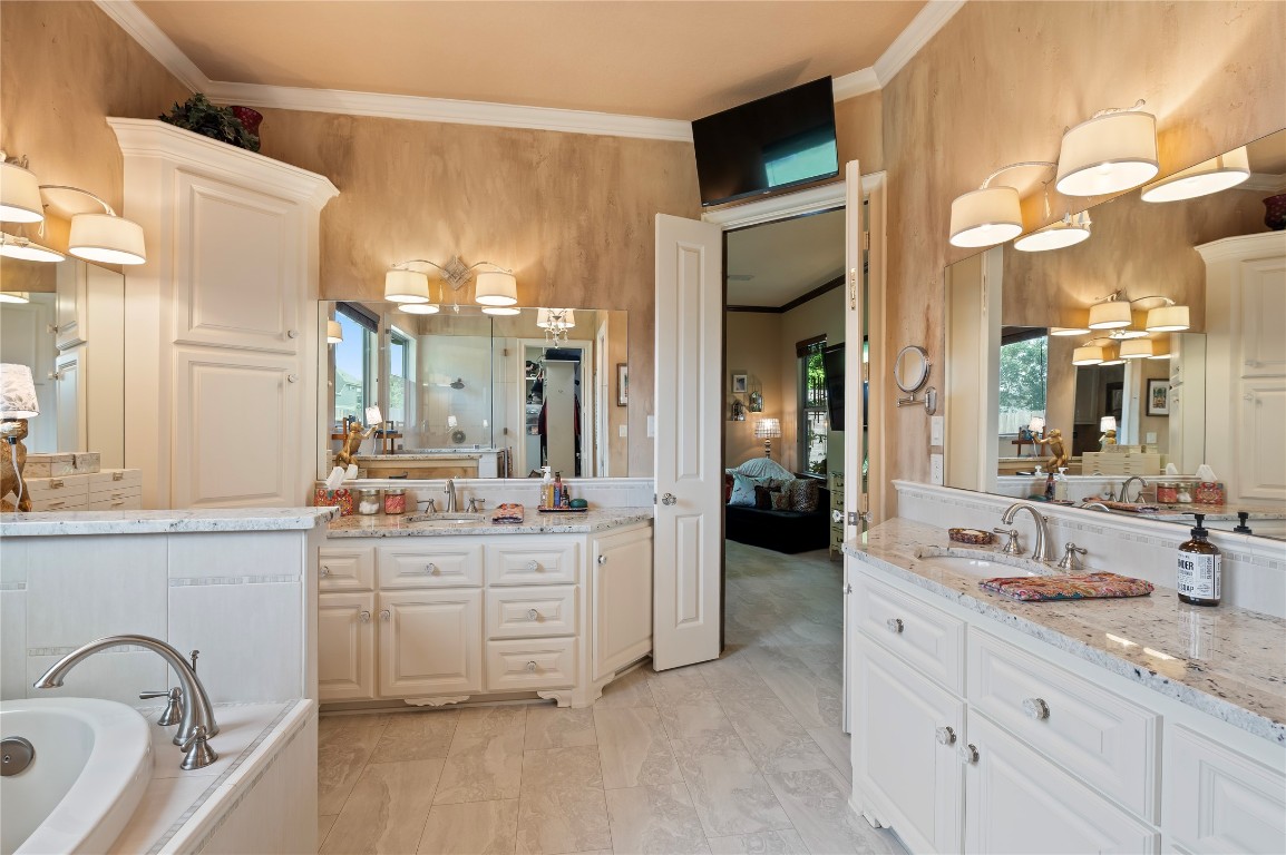 2201 Water Way Seabrook, TX 77586 - Photo 20 of 48 This photo showcases a spacious, elegant bathroom featuring dual sinks with granite countertops, a large mirror, soft wall lighting, and a soaking tub. The room has ample storage with white cabinetry and a warm, inviting color scheme.