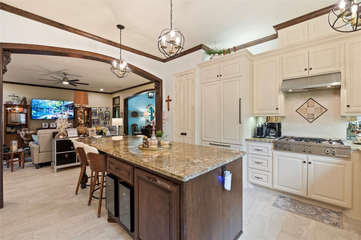 2201 Water Way Seabrook, TX 77586 - Photo 48 of 48 This photo showcases a spacious, elegant kitchen featuring a large granite island with seating, modern appliances, and ample cabinetry. The open floor plan connects to a cozy living area with a ceiling fan and soft lighting, enhancing the home's inviting atmosphere.