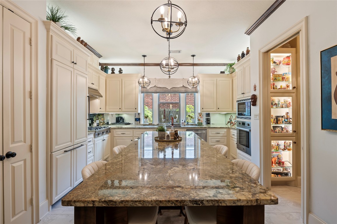 2201 Water Way Seabrook, TX 77586 - Photo 23 of 48 This kitchen features elegant light cabinetry, a large granite island with seating, modern stainless steel appliances, and ample natural light from a window over the sink. There's a convenient walk-in pantry and stylish pendant lighting, creating a warm and functional cooking space.