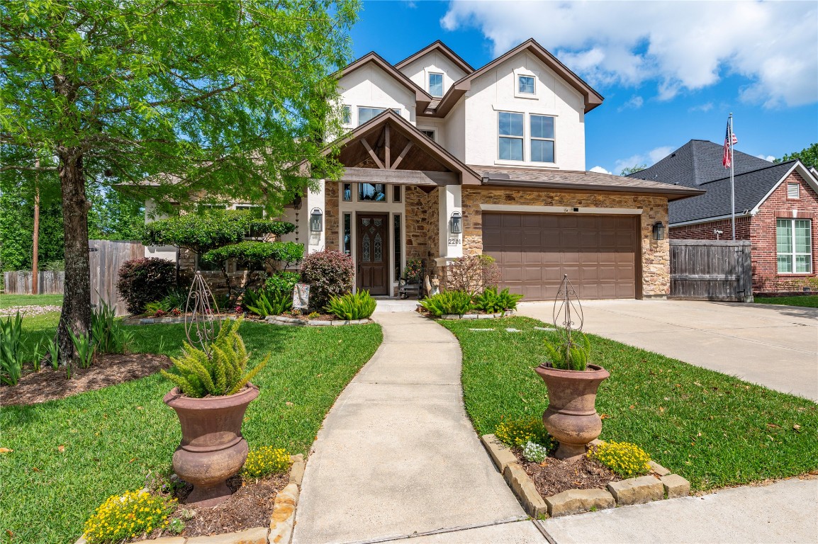 2201 Water Way Seabrook, TX 77586 - Photo 3 of 48 This photo showcases a charming two-story home with a stone and stucco exterior. It features a well-maintained front yard, a paved walkway leading to an inviting entrance, and a spacious driveway with a two-car garage. Lush greenery and decorative planters enhance the curb appeal.