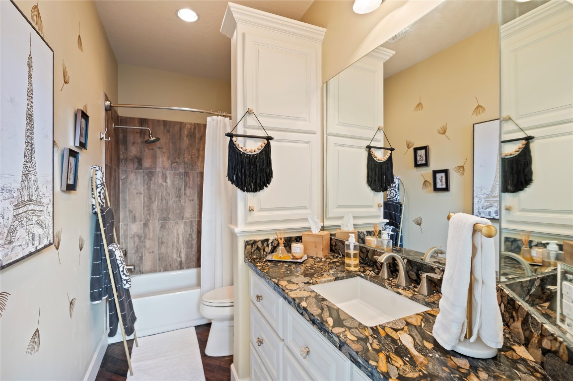 2201 Water Way Seabrook, TX 77586 - Photo 31 of 48 This secondary upstairs bathroom features elegant cabinetry and a stylish granite countertop. It has a modern tub with wood-patterned tiles and decorative wall accents, creating a cozy, sophisticated atmosphere.