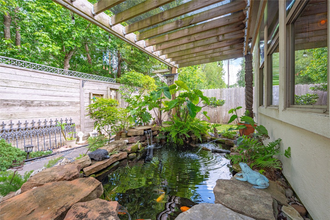2201 Water Way Seabrook, TX 77586 - Photo 36 of 48 This serene backyard features a charming koi pond surrounded by lush greenery and rocks, under a wooden pergola for a peaceful retreat. Nearby, a decorative fence and wooden wall add privacy and character.