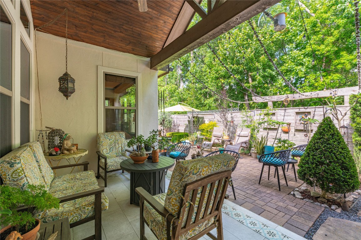 2201 Water Way Seabrook, TX 77586 - Photo 37 of 48 This inviting outdoor space features a cozy covered patio with comfortable seating, decorative lanterns, and lush greenery. The adjacent open patio area offers ample seating and is adorned with string lights, perfect for relaxing or entertaining amidst a serene garden setting.