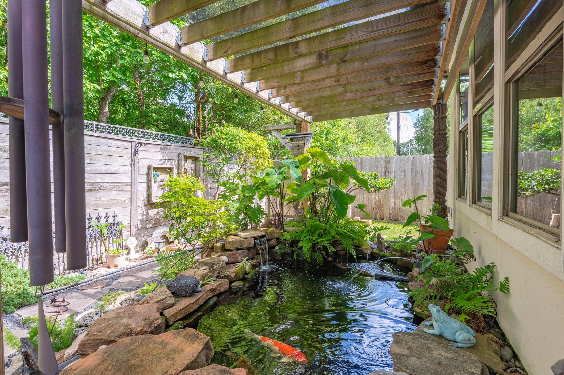 2201 Water Way Seabrook, TX 77586 - Photo 40 of 48 This serene backyard features a koi pond with lush greenery under a wooden pergola. It offers a peaceful retreat with natural stone accents and a charming fence providing privacy and tranquility.