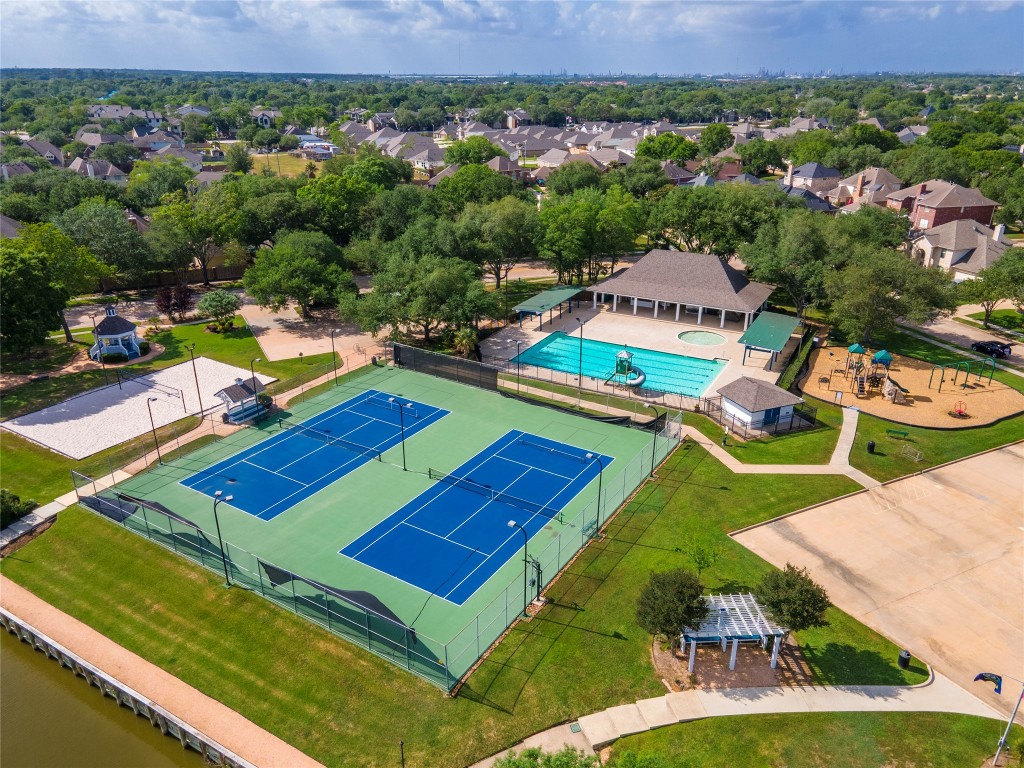 2201 Water Way Seabrook, TX 77586 - Photo 44 of 48 This photo showcases a community recreational area featuring tennis courts, a swimming pool with a covered pavilion, a playground, and a sand volleyball court. It's surrounded by lush greenery and residential homes, offering a vibrant and active neighborhood setting.