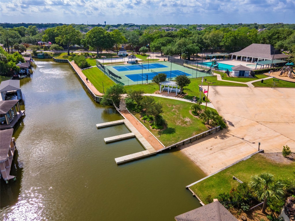 2201 Water Way Seabrook, TX 77586 - Photo 45 of 48 This photo showcases a scenic waterfront community area with a canal, boat docks, tennis courts, a pool, and a playground, surrounded by lush greenery. Ideal for outdoor and recreational activities.