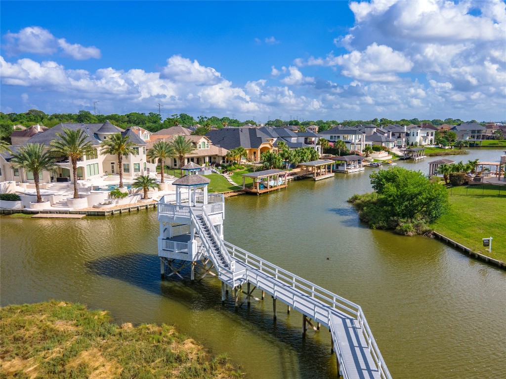 2201 Water Way Seabrook, TX 77586 - Photo 47 of 48 This photo showcases a picturesque waterfront community with luxurious homes, palm trees, and private docks. It features a scenic canal, a prominent viewing deck with stairs, and lush landscaping, all under a bright blue sky. Perfect for those seeking an upscale, tranquil living environment.