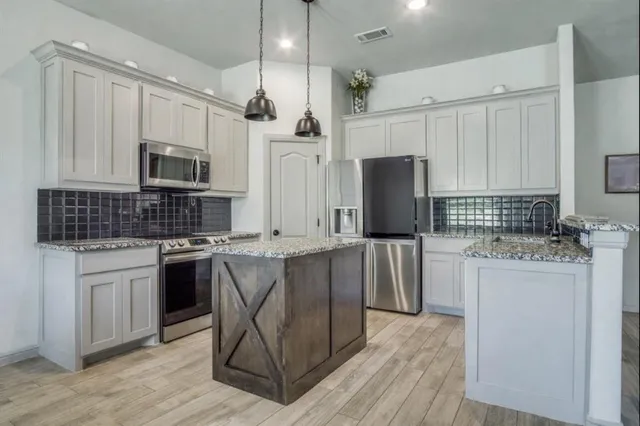 a kitchen with stainless steel appliances granite countertop a stove top oven a refrigerator a sink and white cabinets