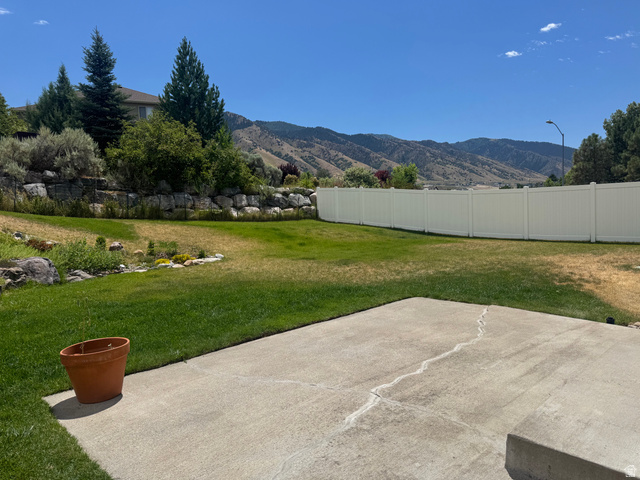 88 Canterbury Lane Logan, UT 84321 - Photo 36 of 37 Expansive backyard featuring a large concrete patio, a durable white vinyl privacy fence, and a terraced rock retaining wall