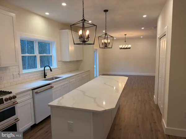 a kitchen with stainless steel appliances a sink a microwave a stove and white cabinets with wooden floor