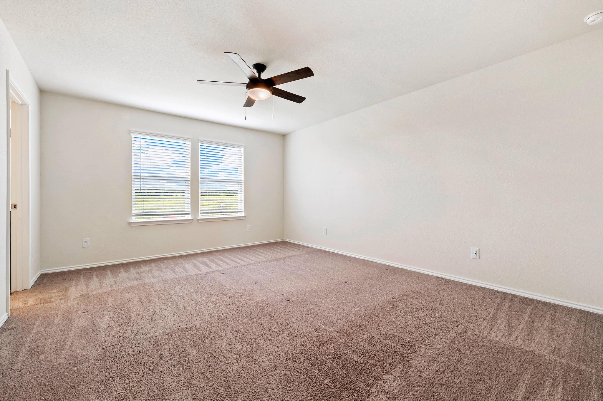 217 Innisfree Road Jarrell, TX 76537 - Photo 12 of 21 A spacious bedroom features plush carpeting and a modern ceiling fan, offering comfortable living.