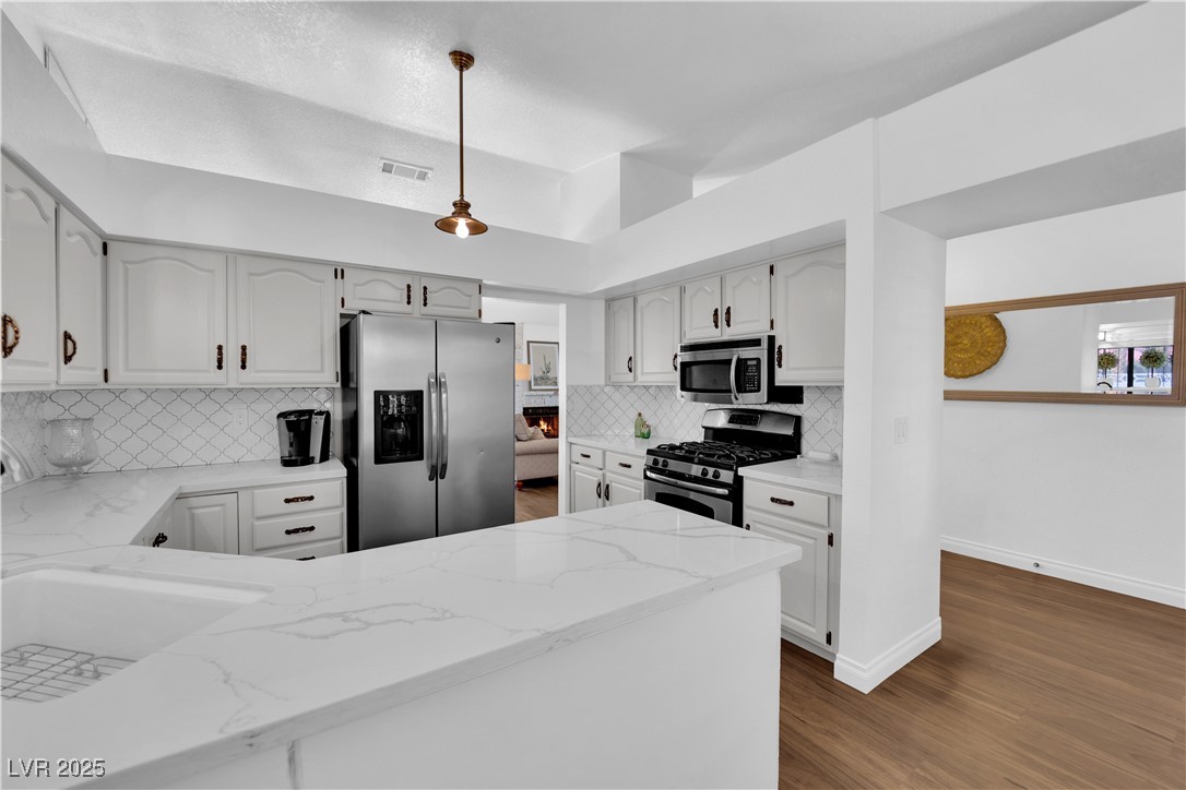 148 Triberg Court Henderson, NV 89074 - Photo 12 of 27 Kitchen featuring dark wood-style flooring, Calcutta quartz countertops, stainless steel appliances, and tasteful backsplash
