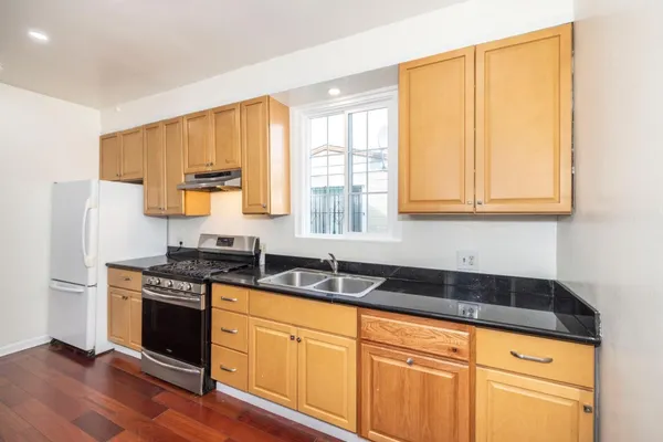 a kitchen with stainless steel appliances granite countertop a stove a sink a refrigerator with white cabinets and wooden floor