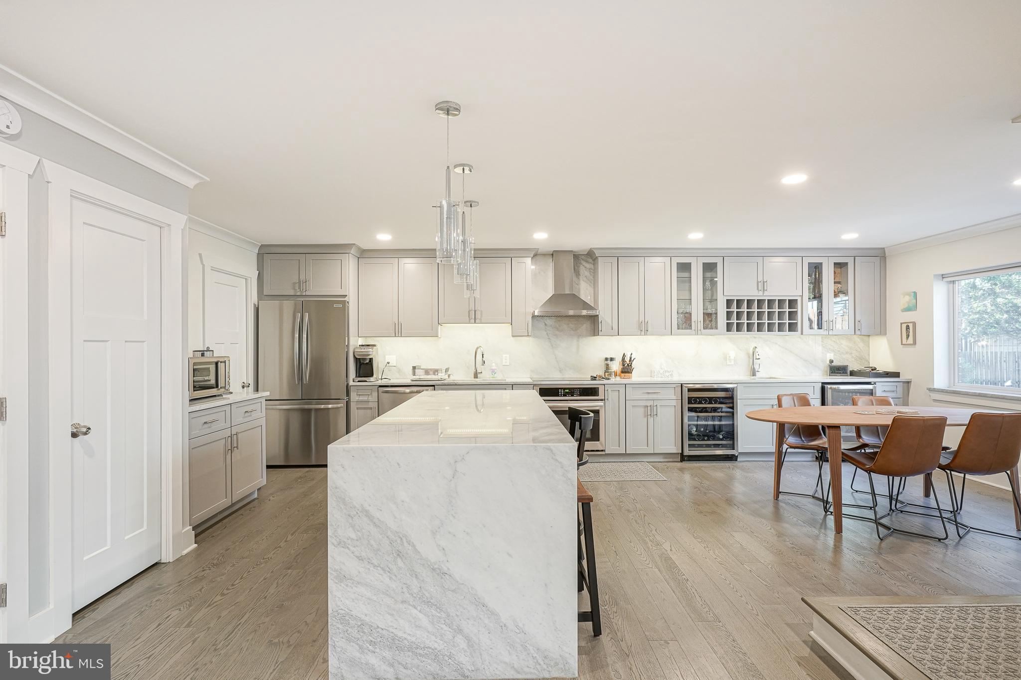 a kitchen with stainless steel appliances kitchen island granite countertop a refrigerator a stove a sink a dining table and chairs with wooden floor