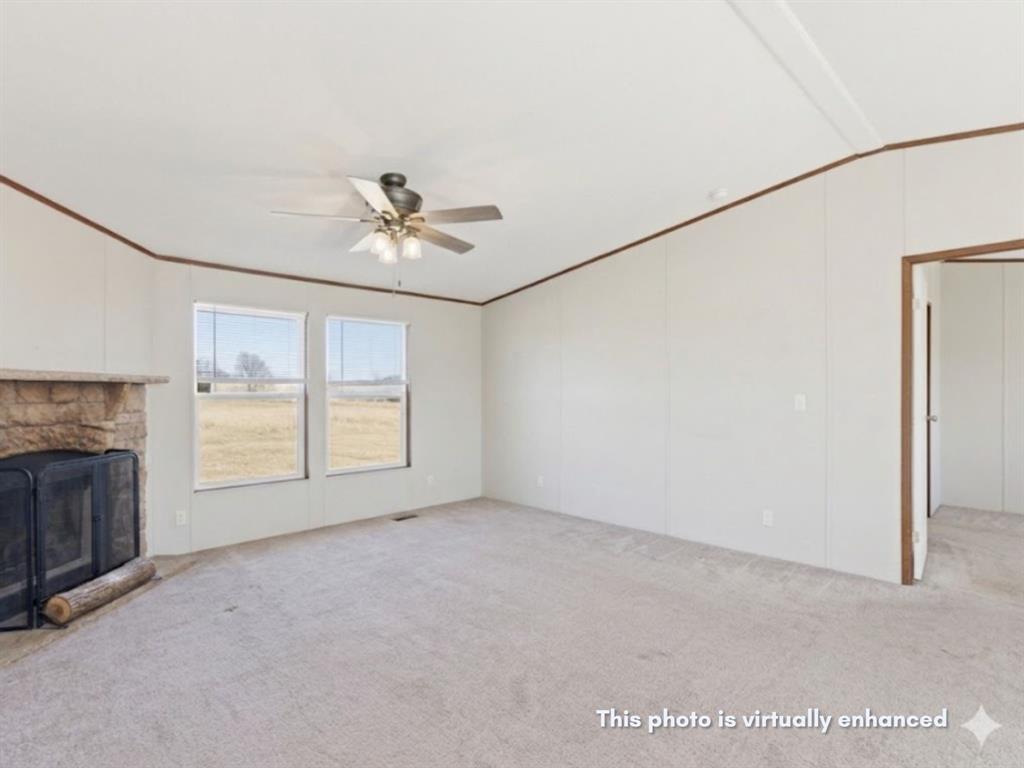 2722 Denver Road Sunset, TX 76270 - Photo 6 of 19 Spacious living area featuring a stone-clad fireplace, two large windows, a ceiling fan with integrated lighting, and neutral carpet flooring