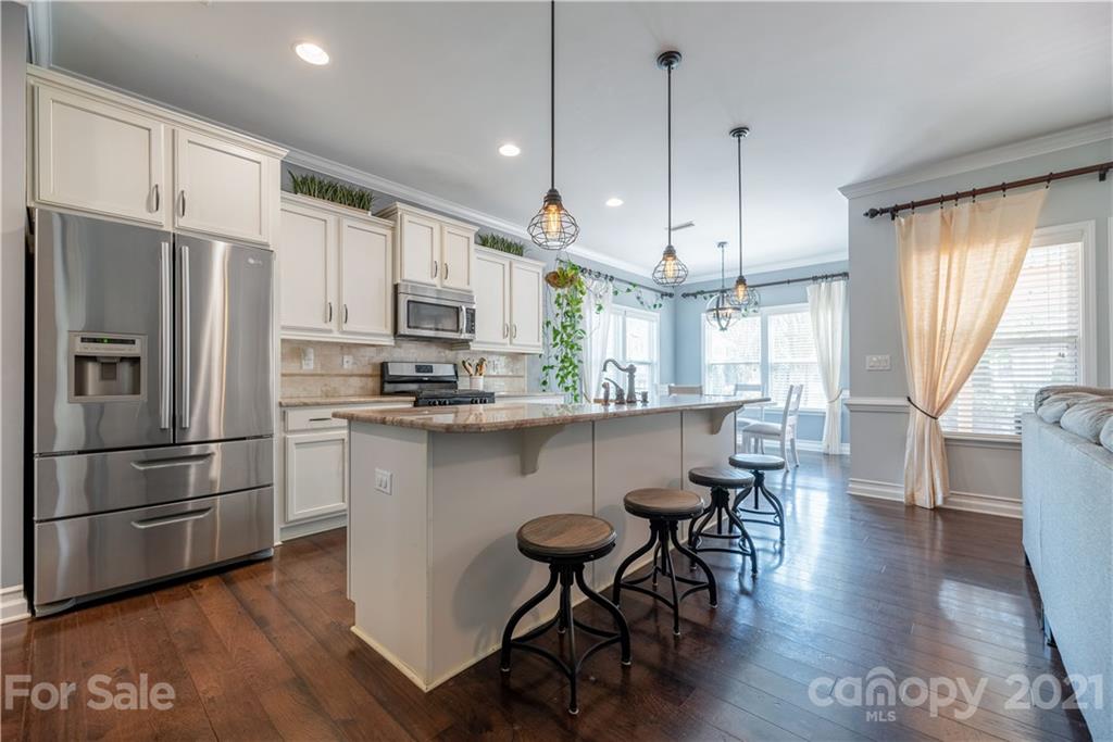 8049 Bryson Road, Unit 117 Indian Land, SC 29707 - Photo 19 of 40 a kitchen with stainless steel appliances granite countertop a refrigerator a stove a sink dishwasher and a dining table with wooden floor
