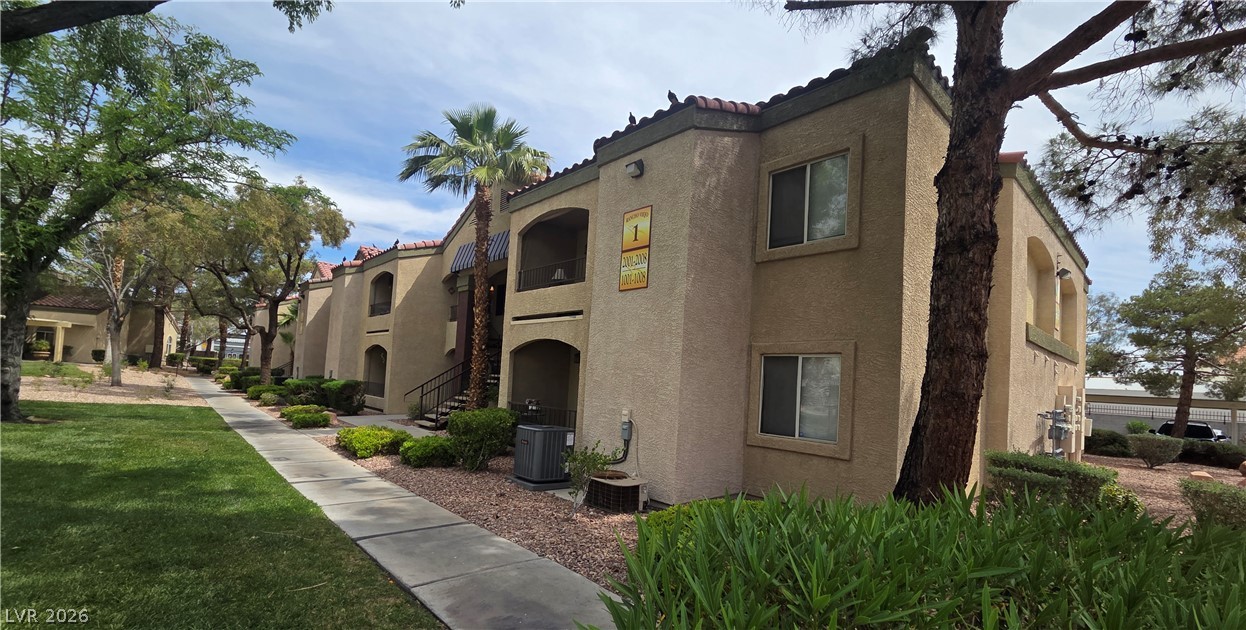 7885 West Flamingo Road, Unit 1008 Las Vegas, NV 89147 - Photo 22 of 29 A terracotta-tiled roof crowns this sand-colored stucco building, bordered by mature trees and a manicured lawn.