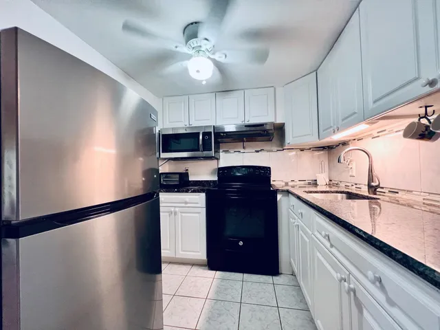 a kitchen with stainless steel appliances granite countertop a refrigerator a sink dishwasher a stove and white cabinets with wooden floor