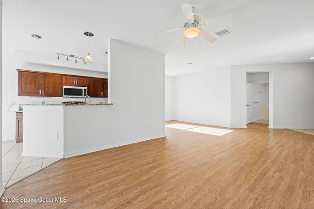 a view of an empty room with wooden floor and a ceiling fan
