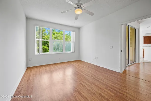 an empty room with wooden floor chandelier fan and windows
