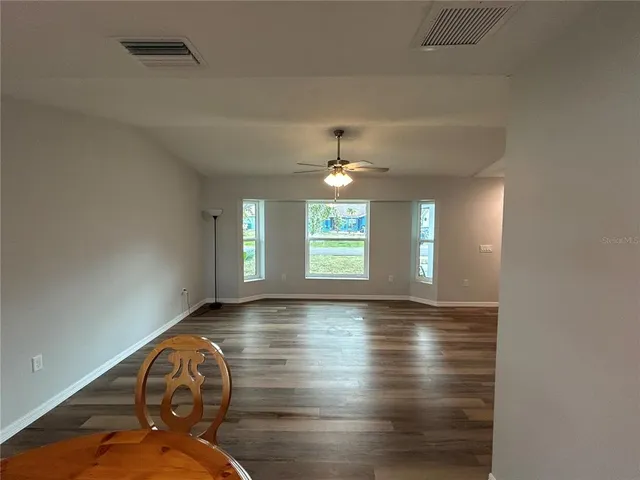 an empty room with wooden floor chandelier fan and windows