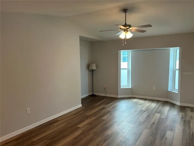 an empty room with wooden floor chandelier fan and windows