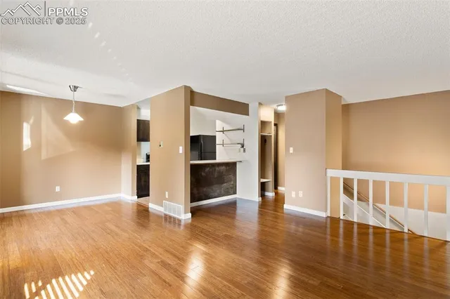 a view of an empty room with wooden floor and a kitchen