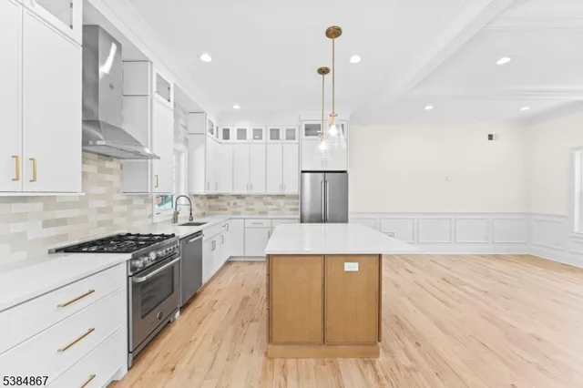 a kitchen with stainless steel appliances granite countertop a stove a sink and white cabinets with wooden floor