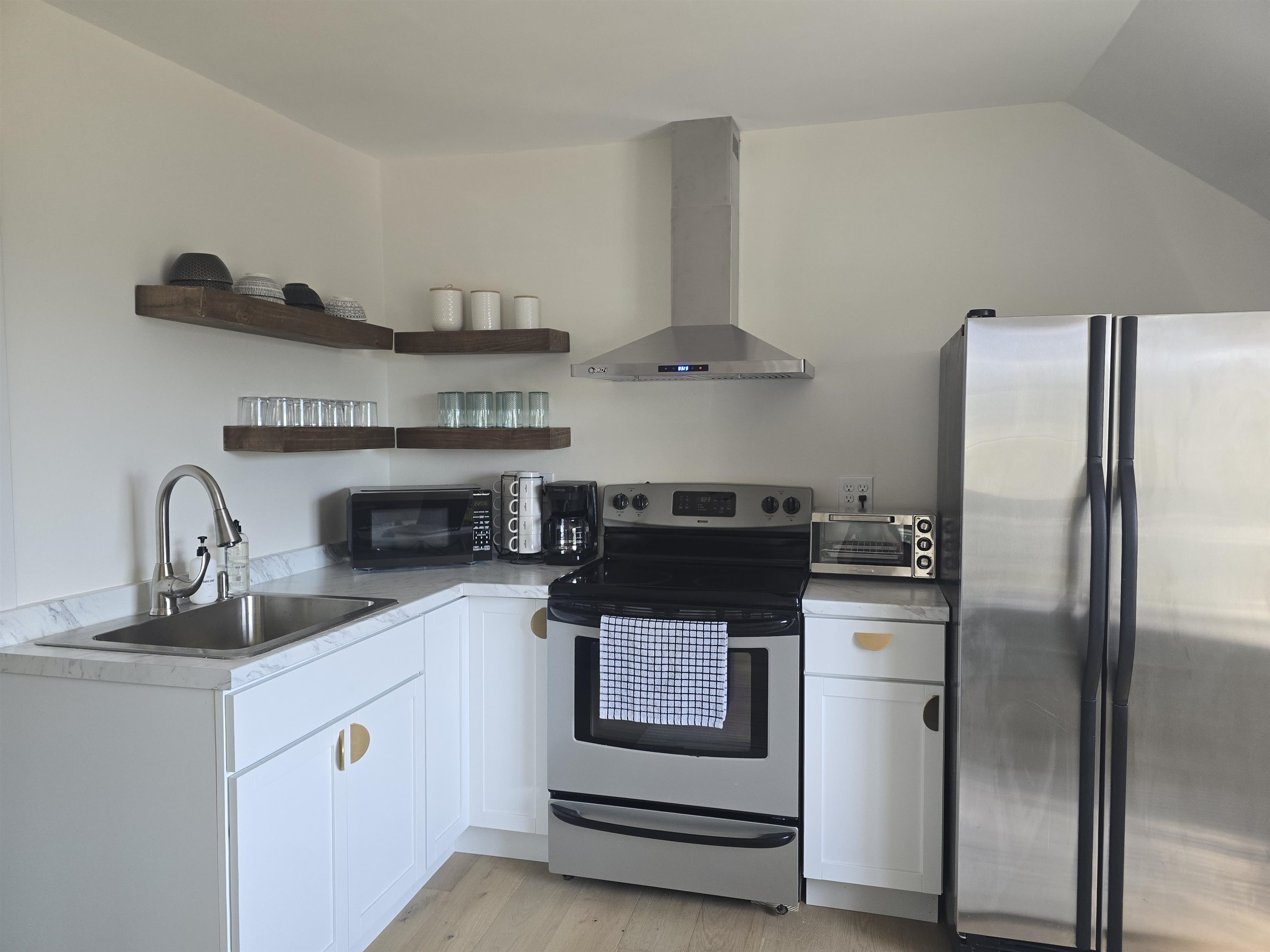 321 Rice Avenue Bayfield, WI 54814 - Photo 8 of 30 Kitchen featuring open shelves, white cabinets, appliances with stainless steel finishes, wall chimney exhaust hood, and light countertops