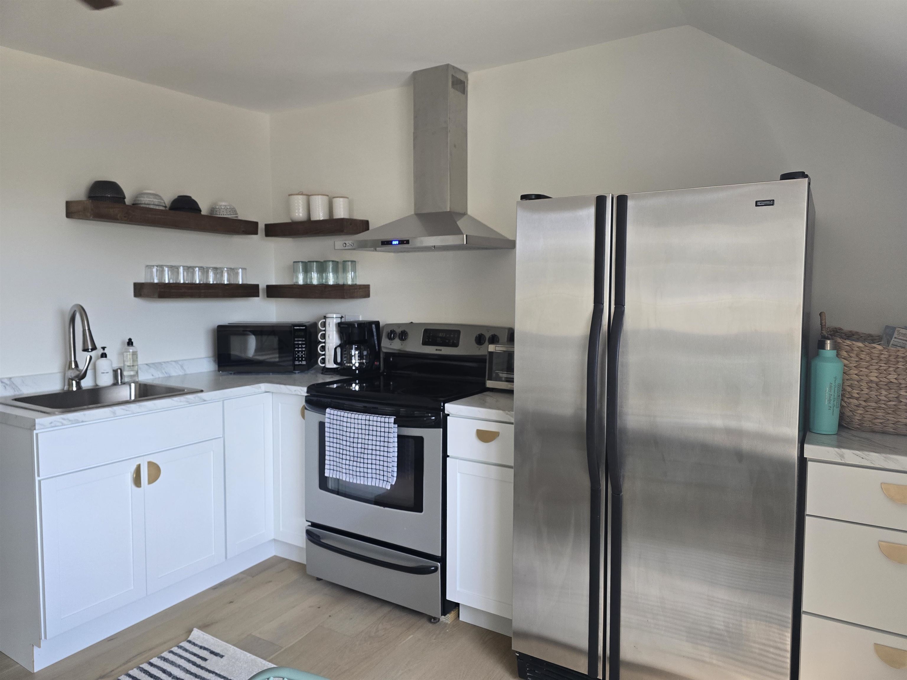 321 Rice Avenue Bayfield, WI 54814 - Photo 10 of 30 Kitchen with stainless steel appliances, white cabinets, wall chimney range hood, open shelves, and light countertops