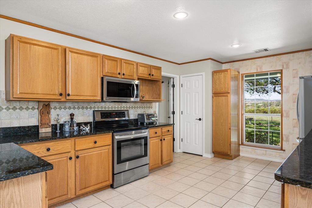 1311 Williamson Road Granbury, TX 76048 - Photo 19 of 40 a kitchen with granite countertop a stove top oven microwave and cabinets