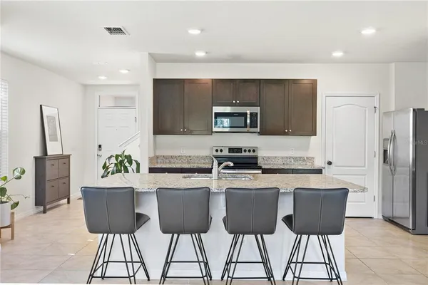 a kitchen with kitchen island granite countertop a stove a sink a refrigerator a dining table and chairs