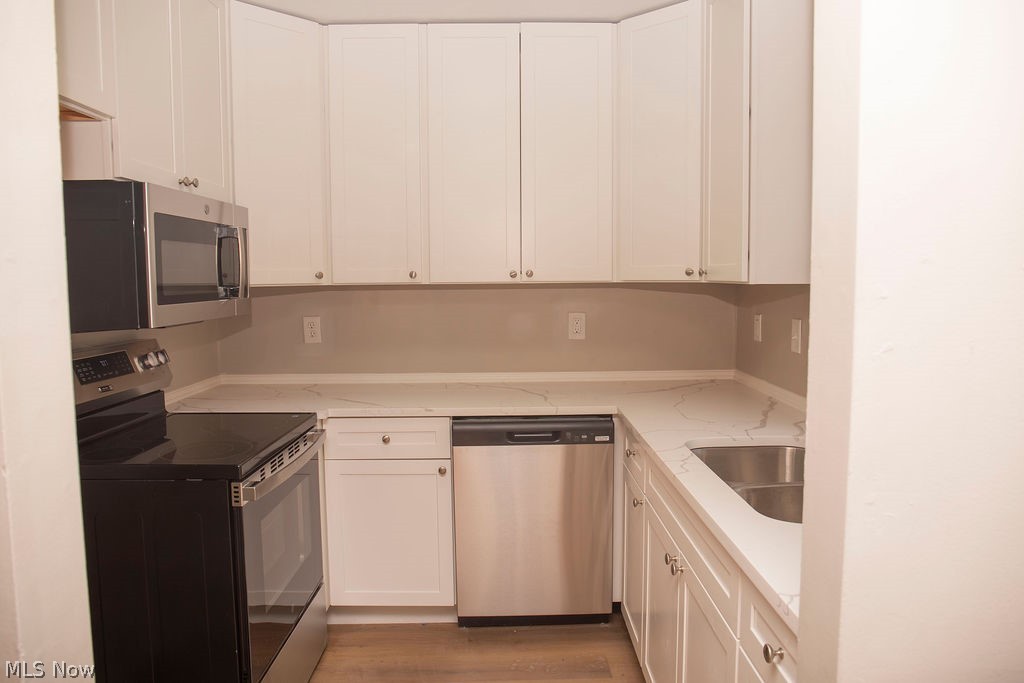 3644 Padanarum Road Geneva, OH 44041 - Photo 5 of 19 Kitchen featuring white cabinetry, light-toned countertops with veining, stainless steel appliances, an undermount double-basin sink, and wood-finish flooring