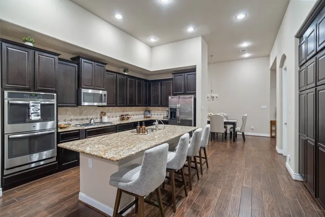 a kitchen with stainless steel appliances granite countertop wooden cabinets a sink a stove a refrigerator and island