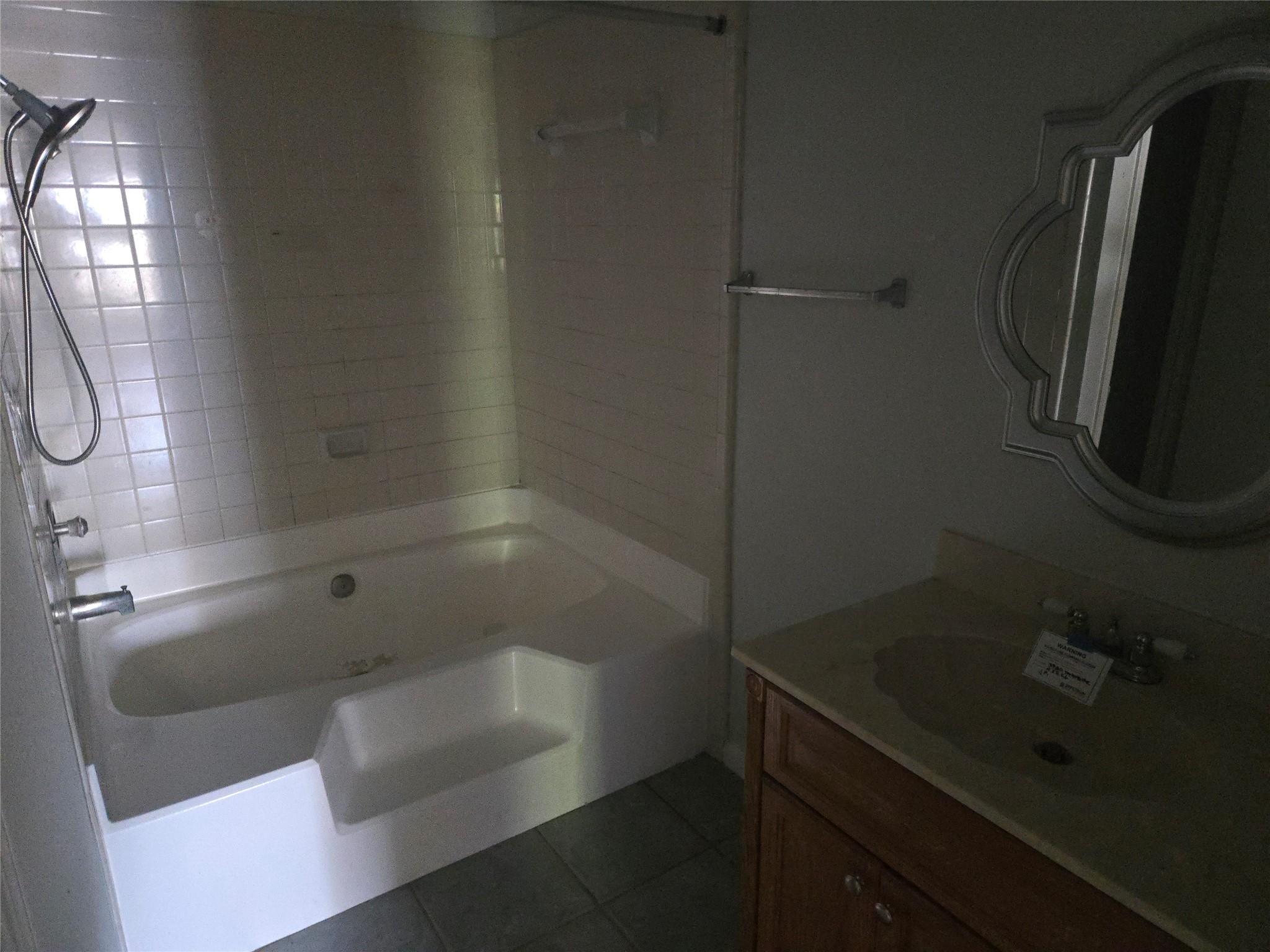 3780 Tanglewilde Street, Unit 501 Houston, TX 77063 - Photo 11 of 26 This bathroom features a tiled shower-tub combo, a single vanity with wood cabinetry, and a decorative mirror, offering a functional space with potential for updates.