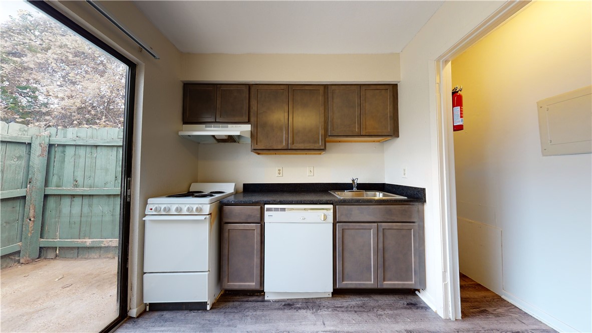 725 Peppertree Drive, Unit 23 Bryan, TX 77801 - Photo 6 of 16 Kitchen featuring white appliances, dark countertops, dark brown cabinets, under cabinet range hood, and light wood-type flooring