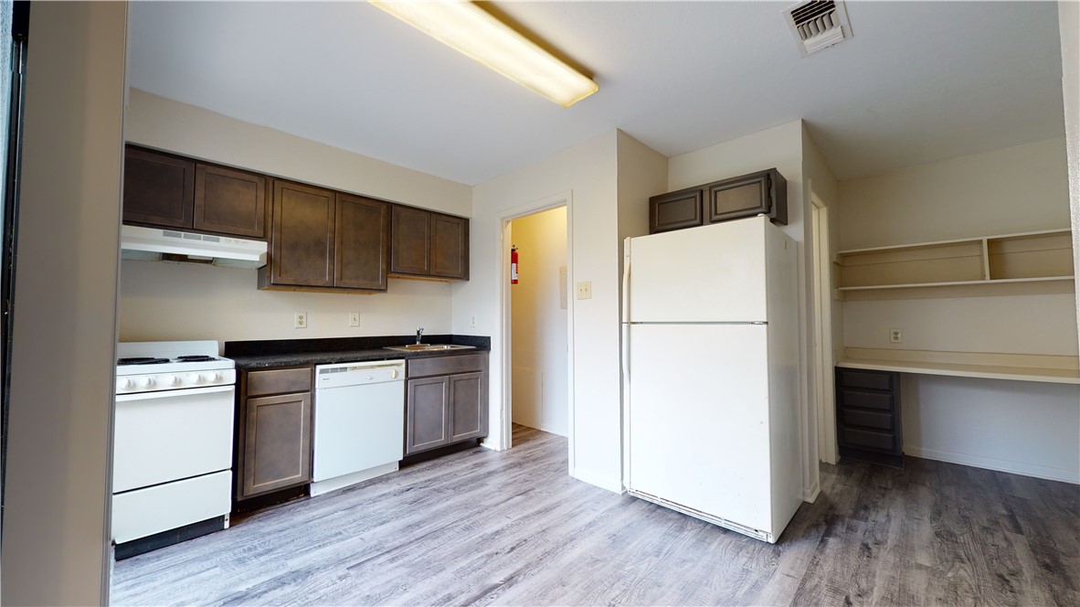 725 Peppertree Drive, Unit 23 Bryan, TX 77801 - Photo 8 of 16 Kitchen with white appliances, dark brown cabinetry, light wood-style floors, under cabinet range hood, and dark countertops