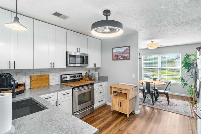 a kitchen with stainless steel appliances granite countertop a stove top oven a sink dishwasher a dining table and chairs with wooden floor