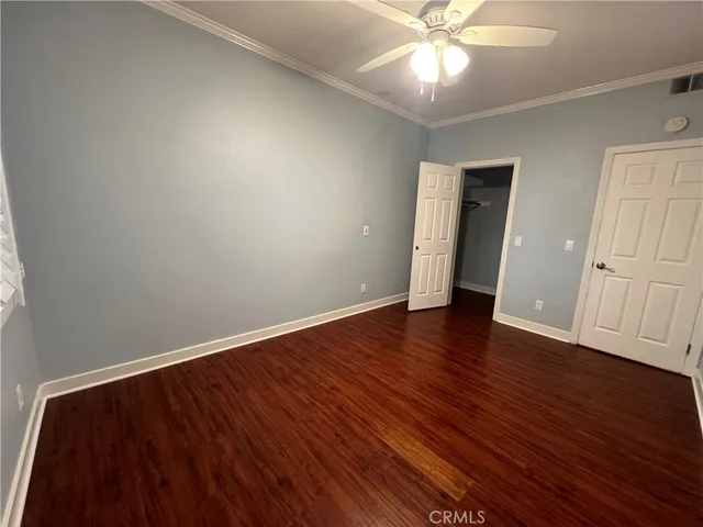 a view of an empty room with wooden floor and a ceiling fan