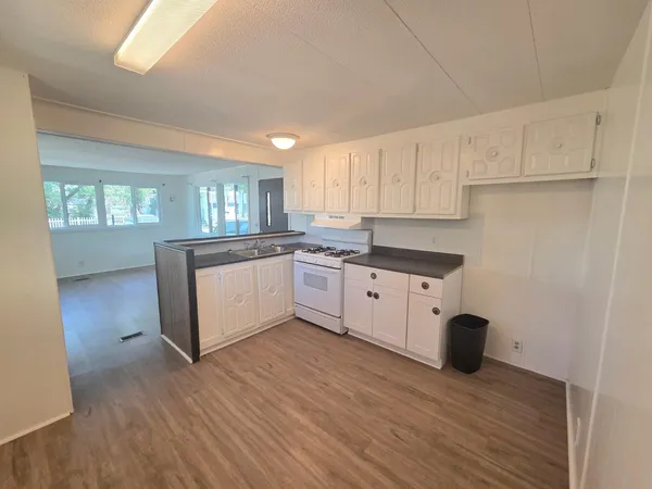 a kitchen with stainless steel appliances granite countertop a stove a sink and white cabinets with wooden floor