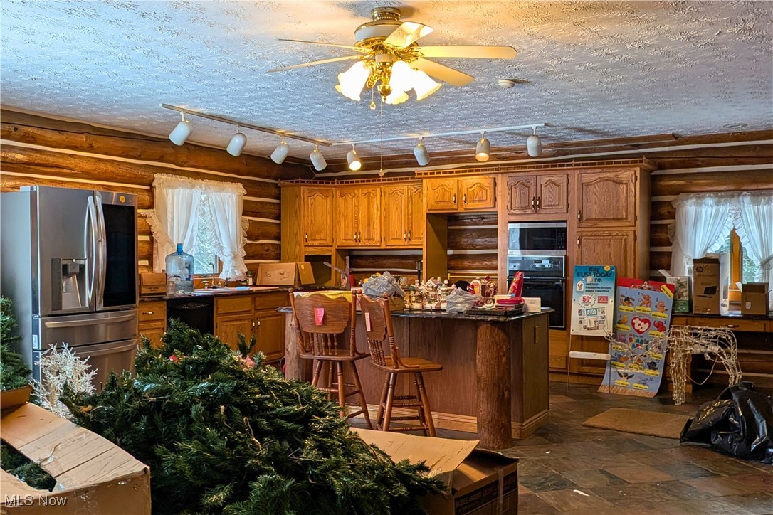 8026 Lee Road Northwest Malvern, OH 44644 - Photo 7 of 44 Kitchen with rustic walls, brown cabinetry, a textured ceiling, black appliances, and a center island