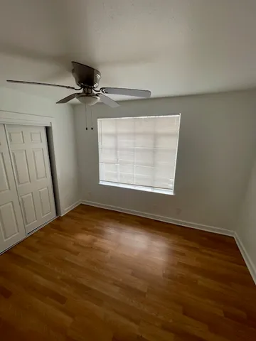 an empty room with wooden floor fan and windows