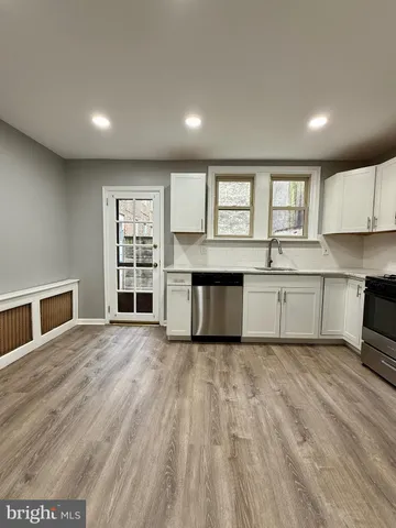 a large kitchen with stainless steel appliances granite countertop a stove top oven a sink dishwasher and white cabinets with wooden floor